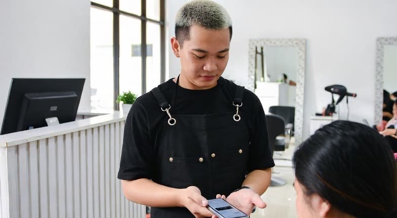 Staf salon memproses pembayaran digital di meja kasir menggunakan ponsel