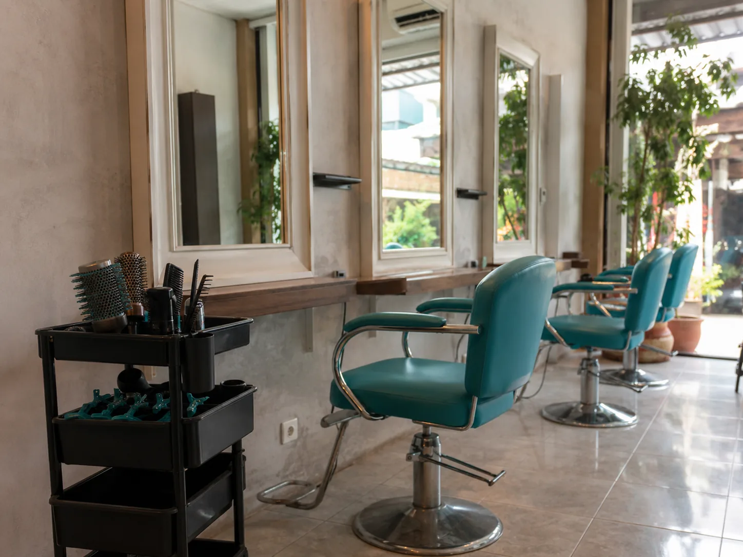 Deretan kursi styling dan cermin di salon rambut, dengan trolley berisi sisir dan jepit rambut di sisi kiri.