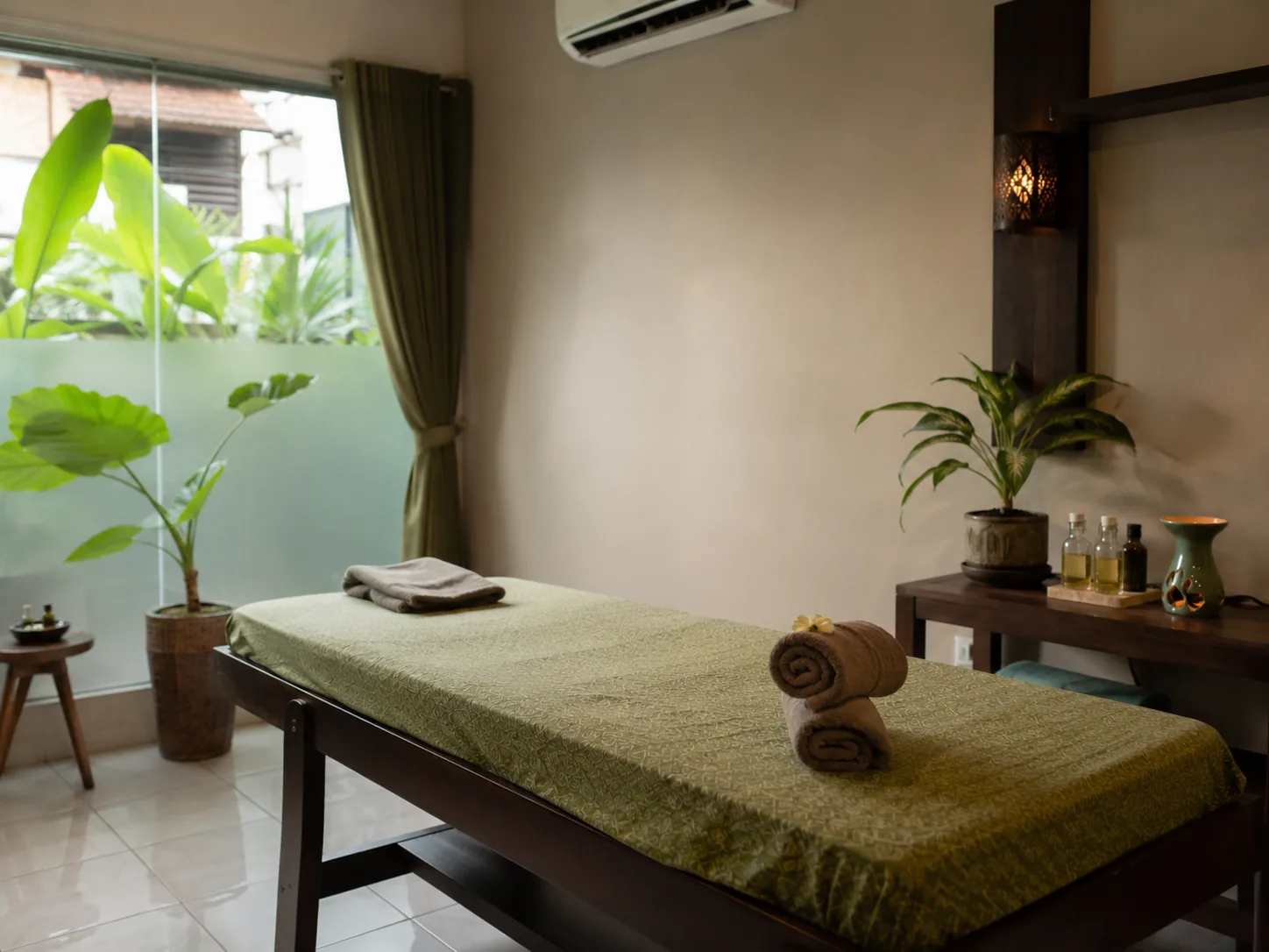 Ruang perawatan spa dengan tempat tidur pijat berlapis kain batik, handuk gulung, dan botol minyak aromaterapi.